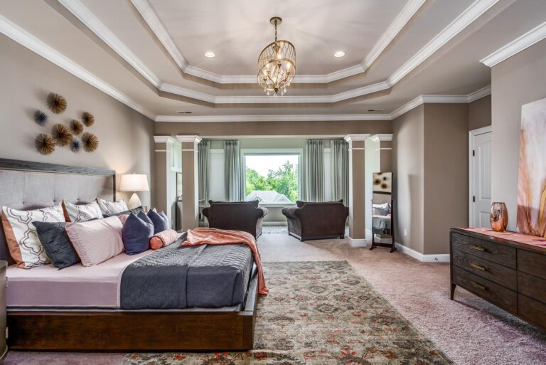 Large bedroom with chandelier, wide comfy chairs, and accent area rug
