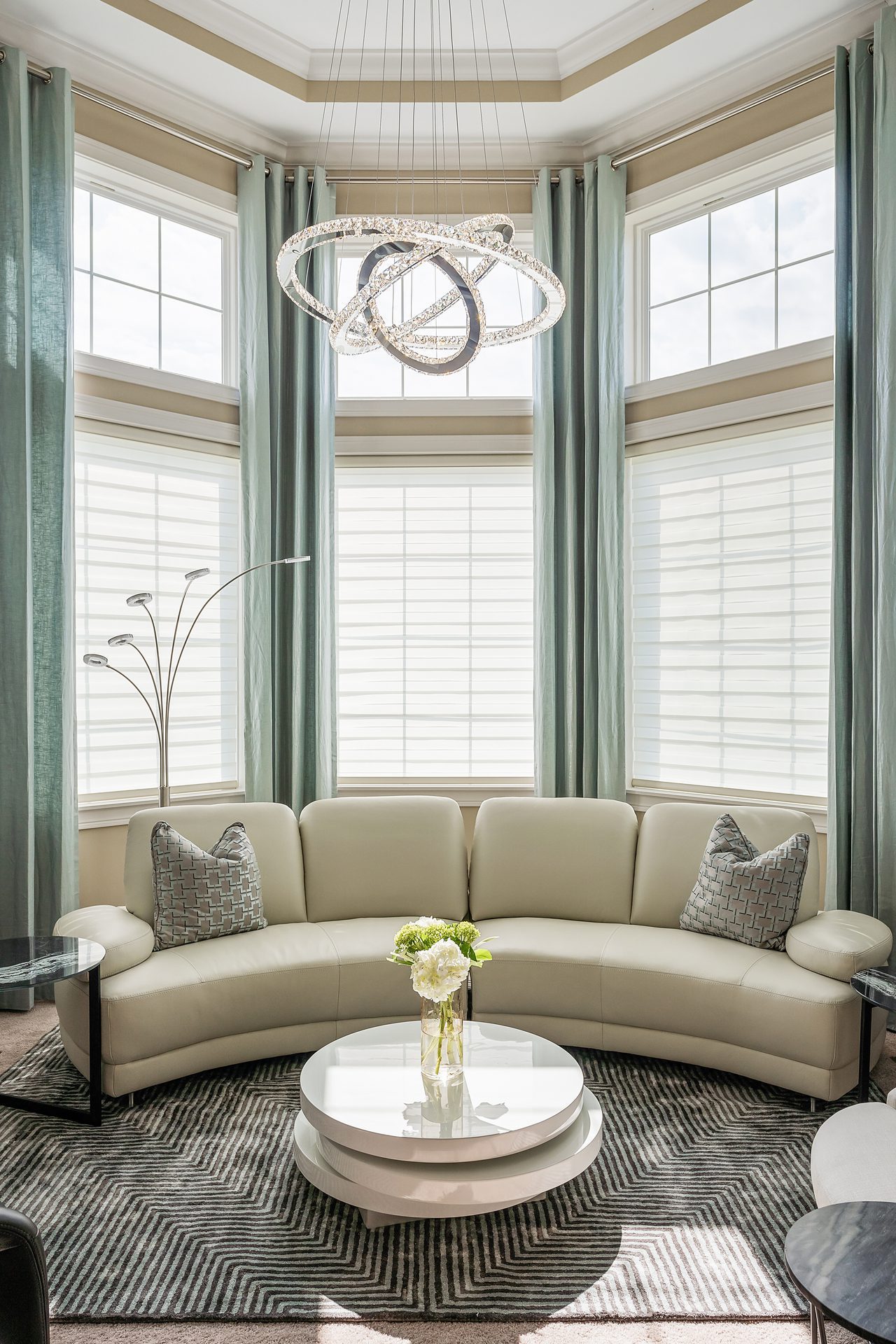 Round couch and tall windows and dynamic, chandelier light featuring intertwining rings.
