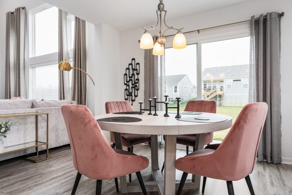 Dining room with four person dining table and chairs. Pink accents, chandelier lamp, and modern decor