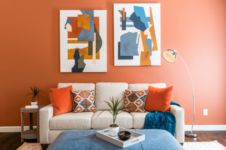 living room with bright orange walls, abstract artwork, and beige sofa with throw pillows